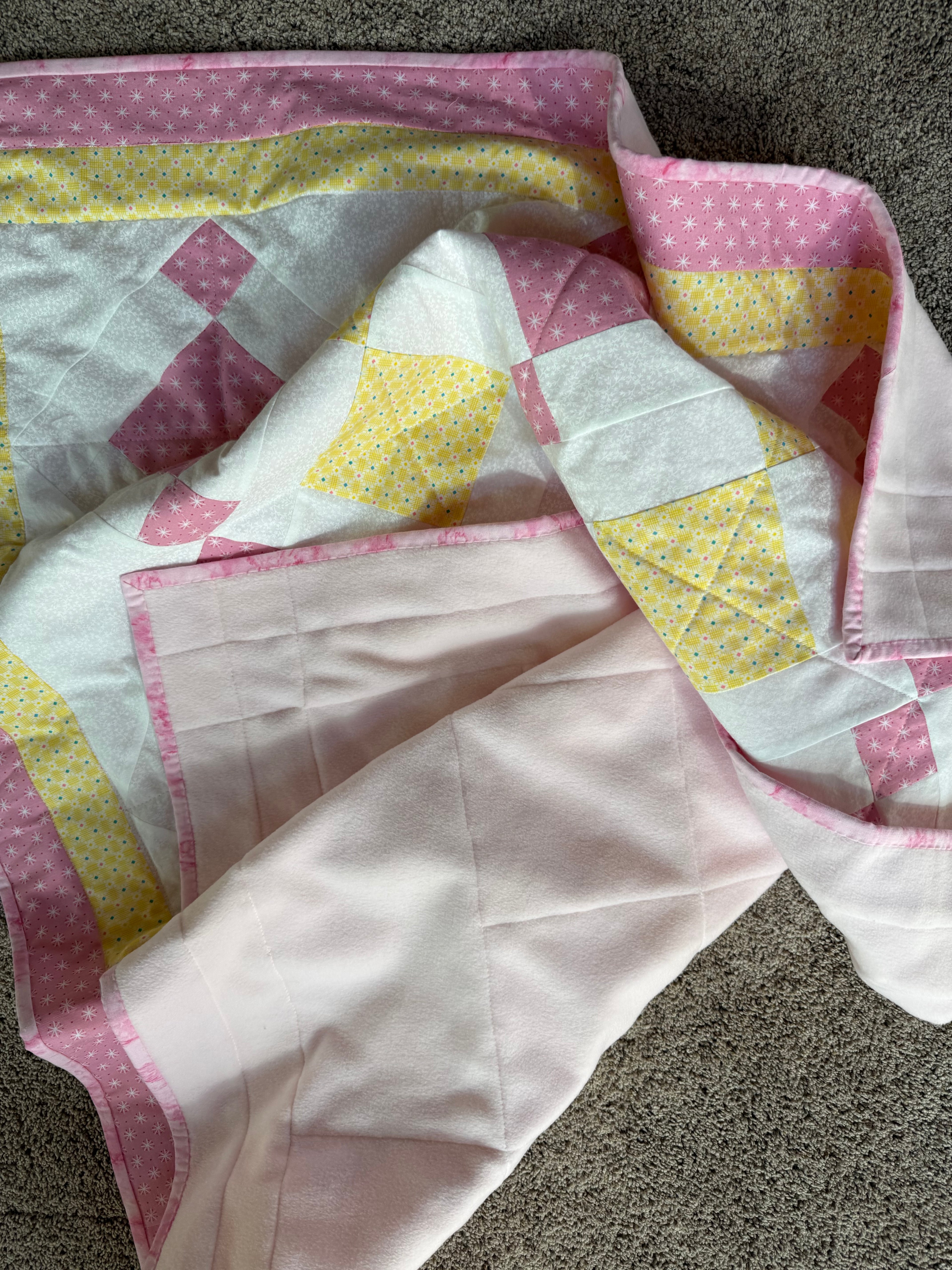Handmade pink and yellow baby quilt in soft cotton, perfect baby gift.  Photo shows how soft and pliable this quilt is. By Oak & Thread Quilts