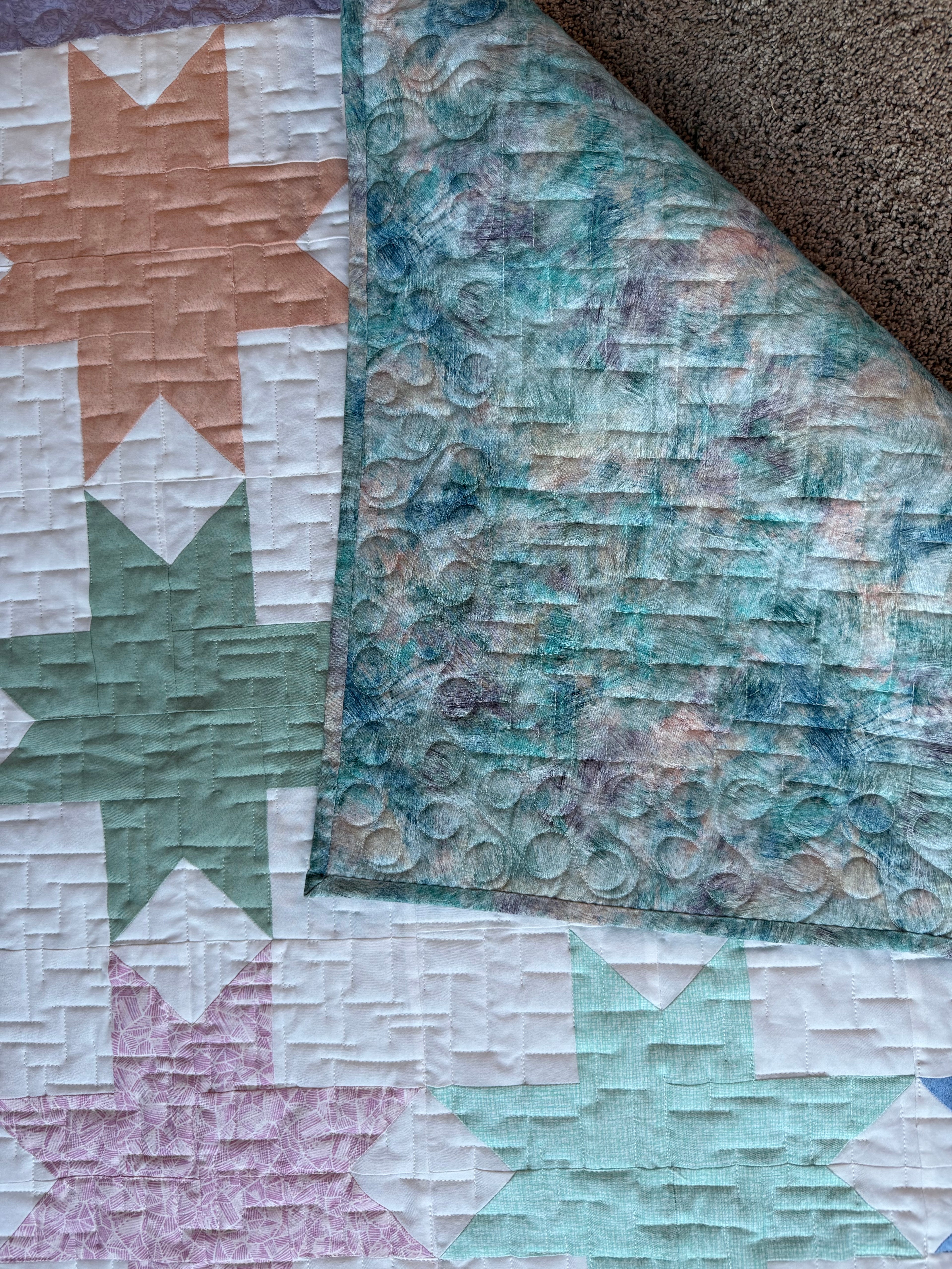 Handmade pastel star baby quilt showing multi colored backing fabric and quilting 