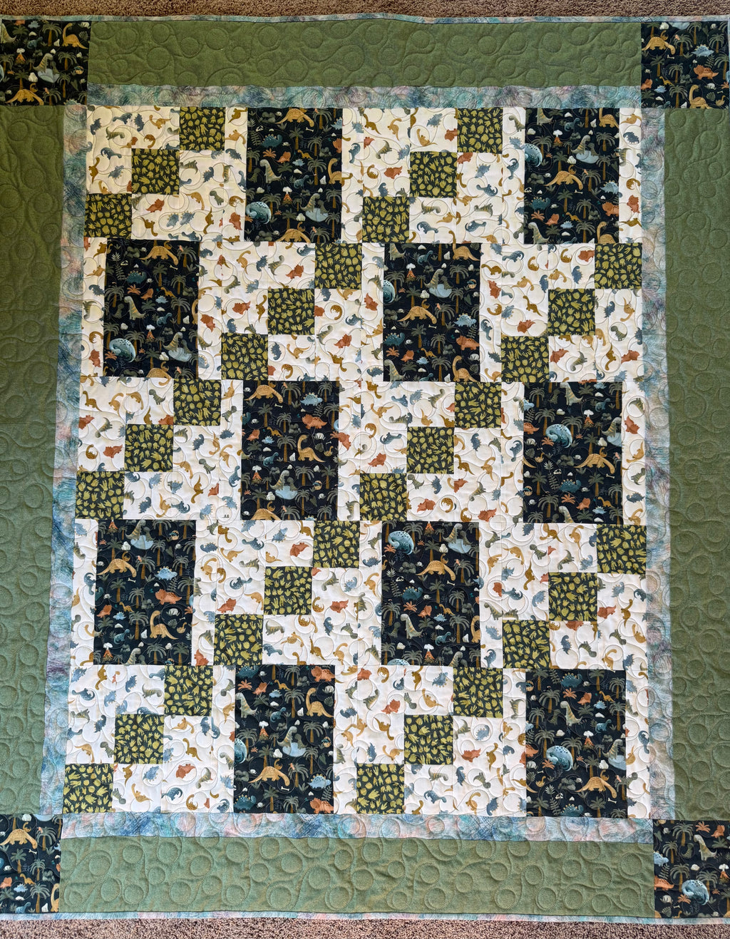 Quilt with various dinosaur fabrics in greens and blues