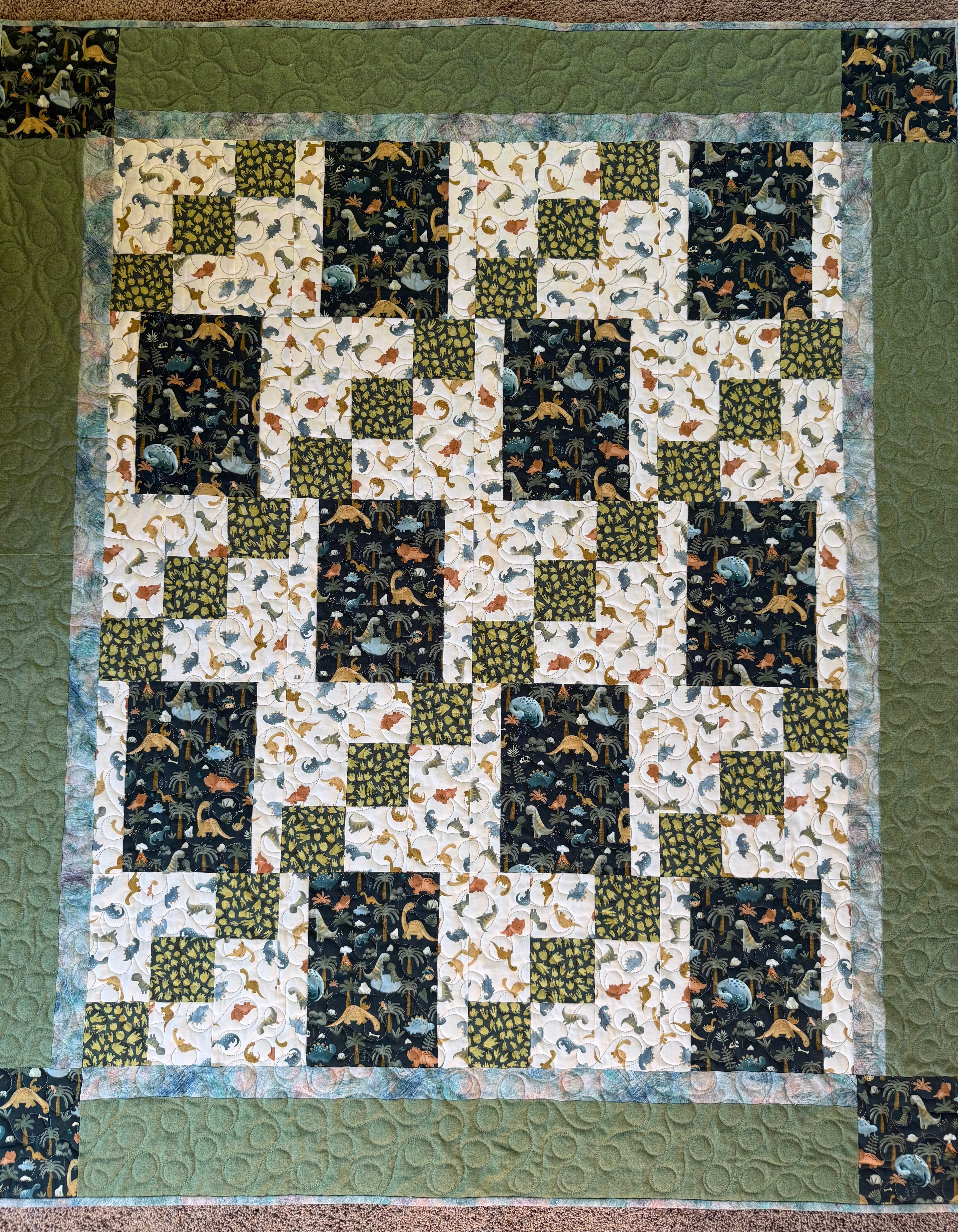 Quilt with various dinosaur fabrics in greens and blues